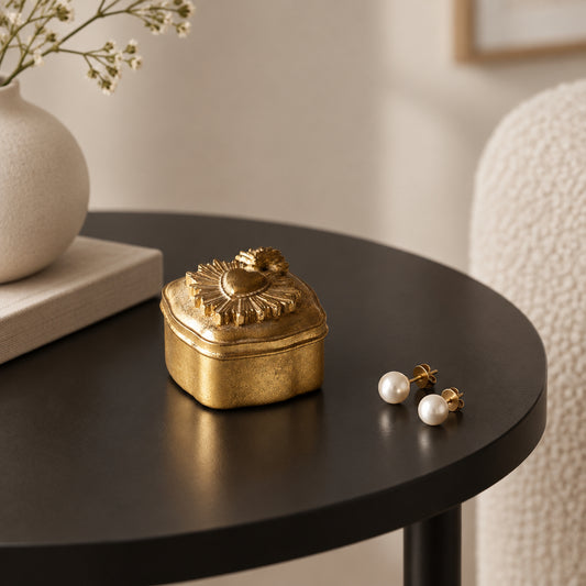 A small ornate gold-colored metal keepsake box with a decorative sunburst lid, resting on a white marble tabletop.