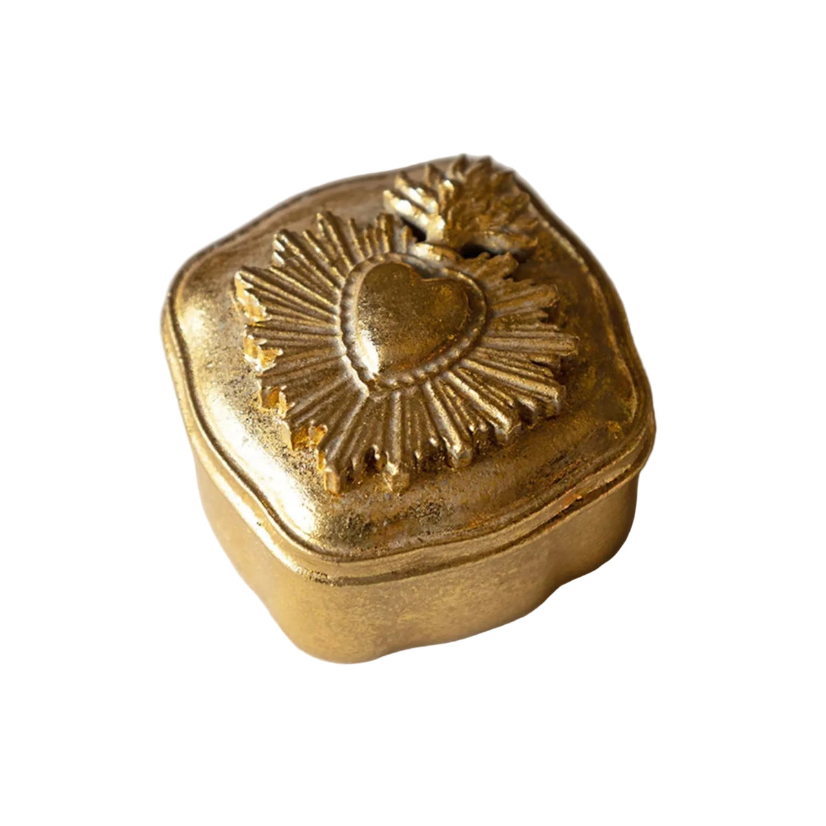 A small decorative gold-toned metal box with a hinged lid, featuring an embossed Sacred Heart design with a leaf on top, set against a light marble background.