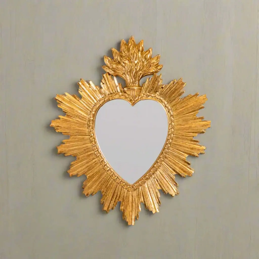 Decorative gold mirror with heart shape and sunburst design on a white background
