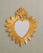 Decorative gold mirror with heart shape and sunburst design on a white background