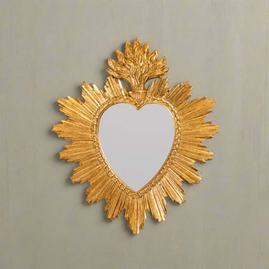 Decorative gold mirror with heart shape and sunburst design on a white background