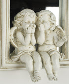 Two angel statues in front of a mirror with a decorative frame.