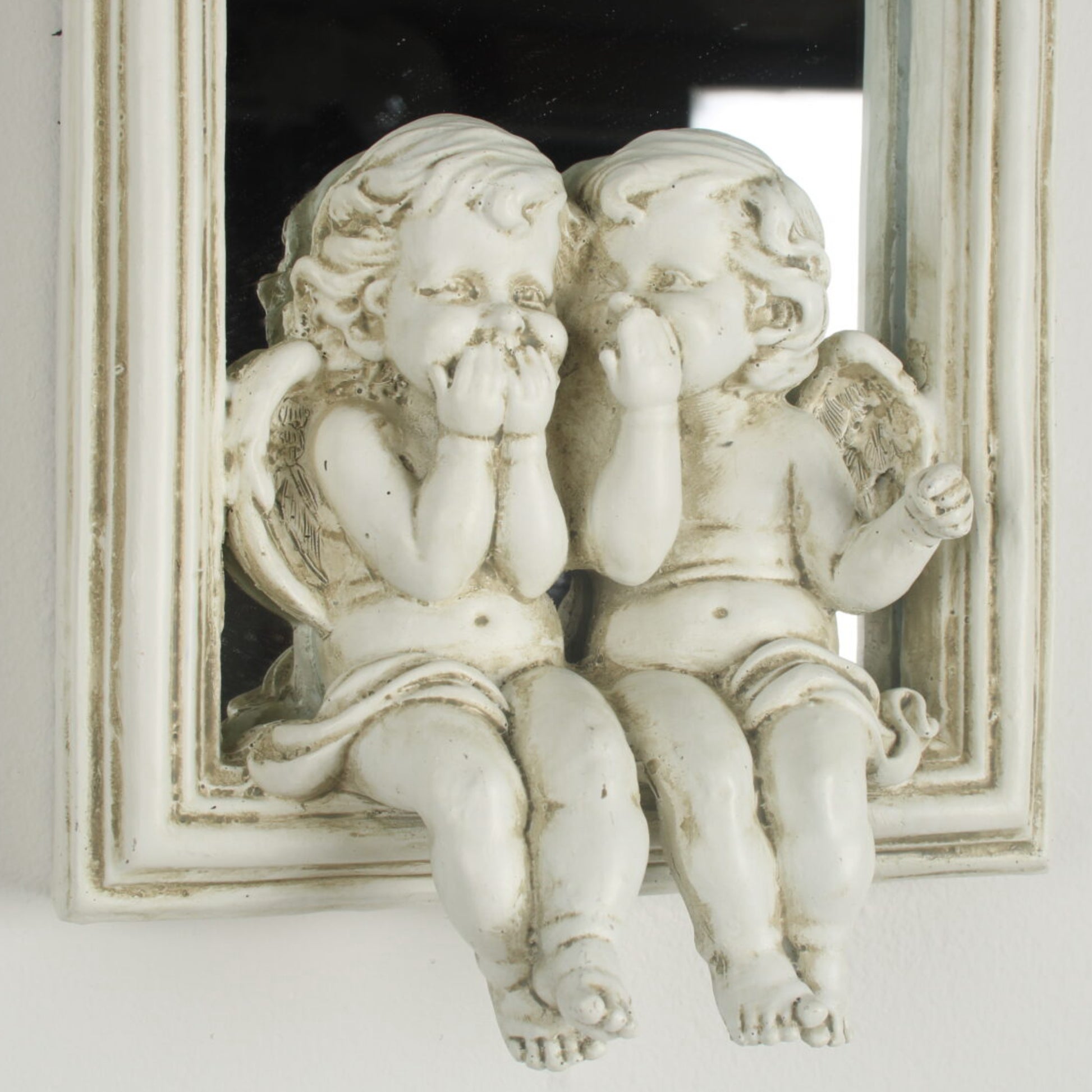Two angel statues in front of a mirror with a decorative frame.