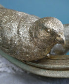 Bronze sculpture of a bird perched on a branch with a blue background