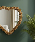 Heart-shaped mirror with floral frame on a green wall next to a plant