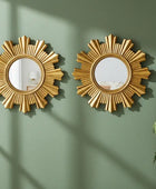 Two gold sunburst mirrors on a green wall with a plant to the right.