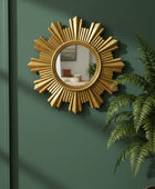 Gold sunburst mirror on a green wall with a plant to the right