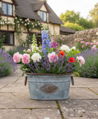 Floral arrangement in a metal bucket on a stone path with a garden and house in the background