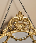Decorative gold mirror with intricate designs and a chain on a white background