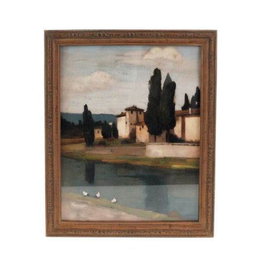 A framed landscape painting depicting a Tuscan scene with cypress trees, a river, and buildings under a cloudy sky, enclosed in a rustic brown wooden frame.