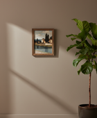 A small framed landscape painting hangs on a warm beige wall, with a large green potted plant in a dark pot to the right and sunlight casting shadows across the wall.