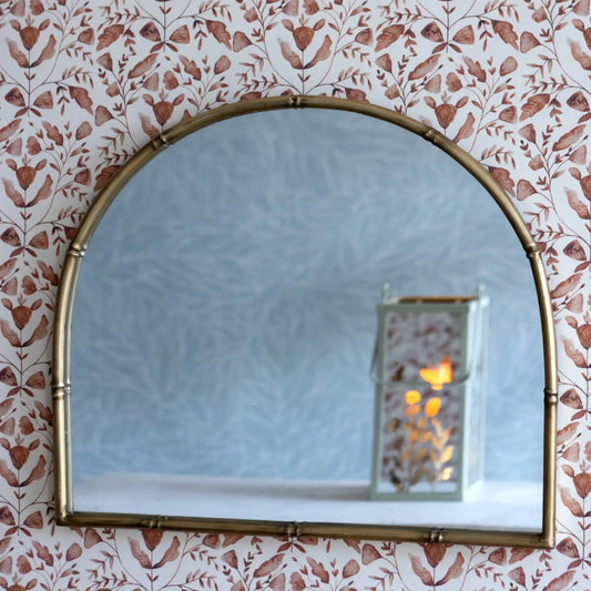 Gold-framed mirror on a wall with floral wallpaper