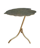 A leaf-shaped side table with a textured metallic gold top and a curved tripod base, set against a dark teal wall and wooden floor.
