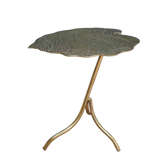 A leaf-shaped side table with a textured metallic gold top and a curved tripod base, set against a dark teal wall and wooden floor.