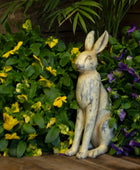 Decorative rabbit statue in front of green foliage with yellow and purple flowers