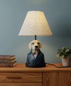 Dog-shaped lamp on a wooden surface with books and a plant against a gray wall.