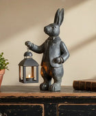Decorative rabbit figurine with a lantern, potted plant, and book on a wooden surface.