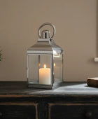 Silver lantern with a candle on a wooden surface against a beige wall