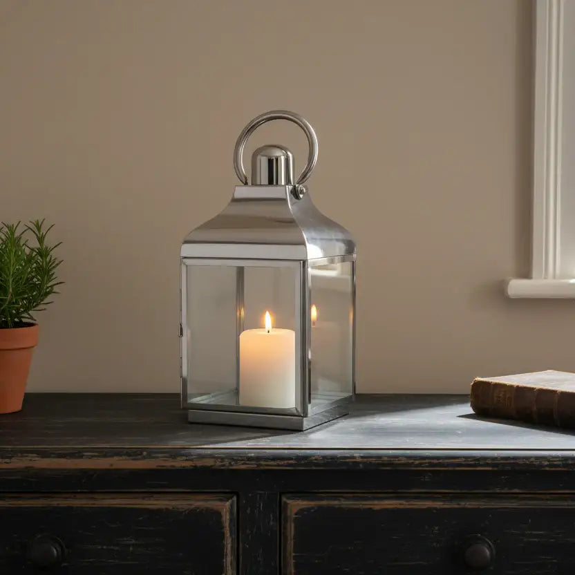 Silver lantern with a candle on a wooden surface against a beige wall