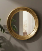 Round gold-framed mirror on a wall with a plant to the left