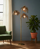 Gold leaf floor lamp in a room with a green chair and potted plant.