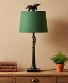 Decorative lamp with green shade on a wooden surface with books and a plant.