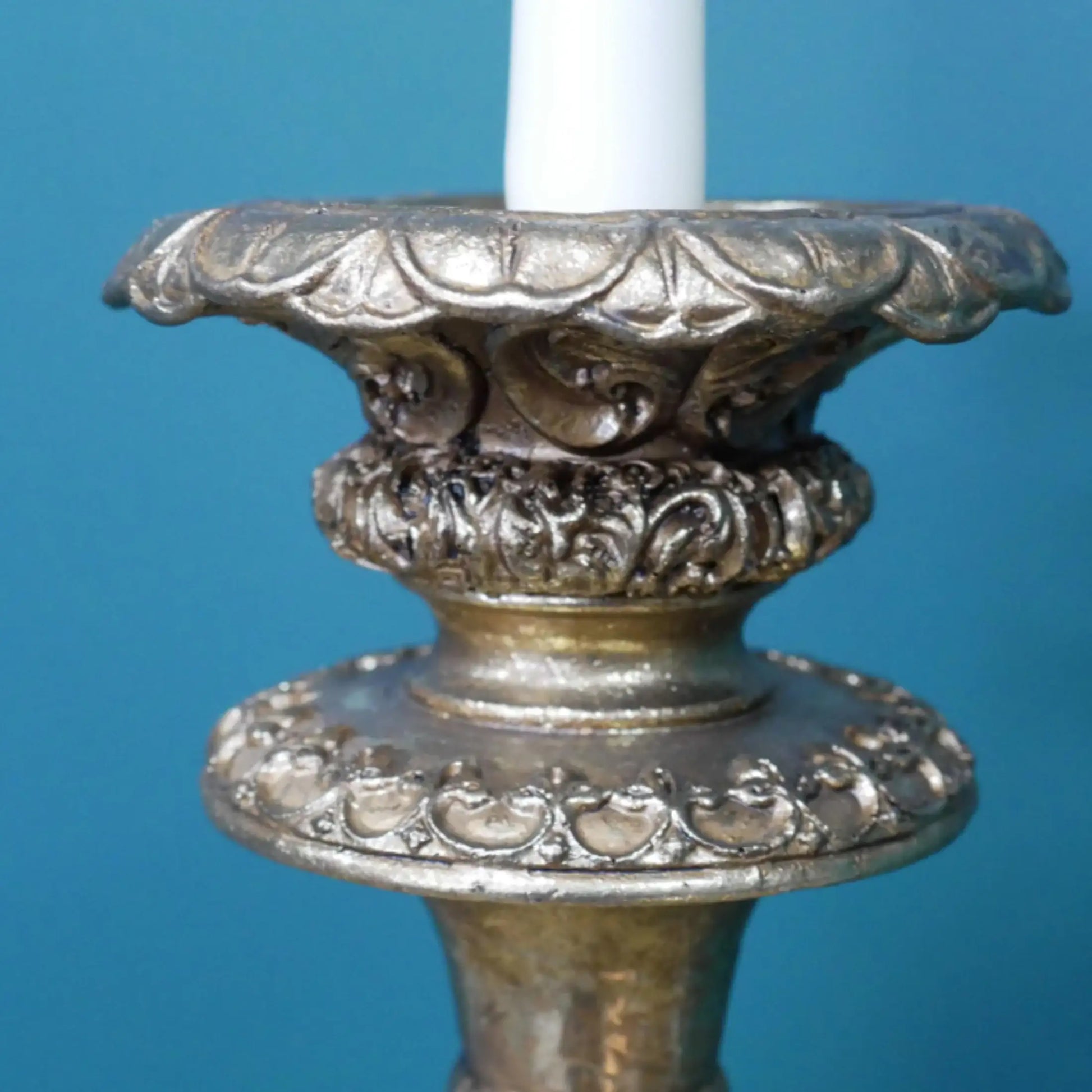 Decorative silver candle holder with a white candle against a blue background