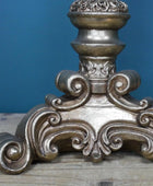 Decorative metal finial with intricate designs on a wooden surface against a blue background