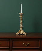 Decorative gold candlestick with a white candle on a wooden dresser against a green wall
