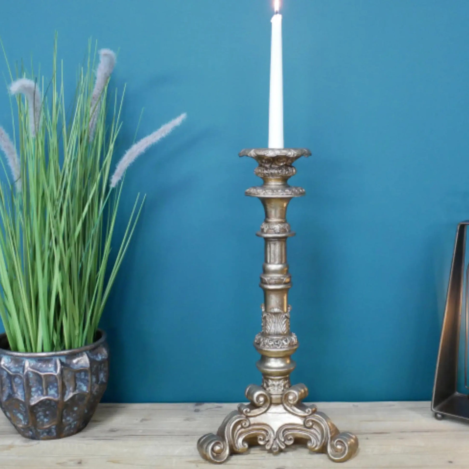Decorative candlestick with a candle on a wooden surface against a blue wall