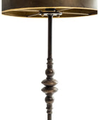 A close-up of a floor lamp with a dark metal turned-wood style stem, a drum shade, and a warm brass-toned inner lining, shown against a plain white background.