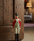 Figurine of a soldier in uniform standing against a wooden wall.