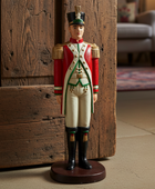 Decorative figurine of a soldier in uniform standing against a wooden wall.