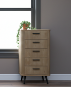 Wooden dresser with multiple drawers against a gray wall with a window.