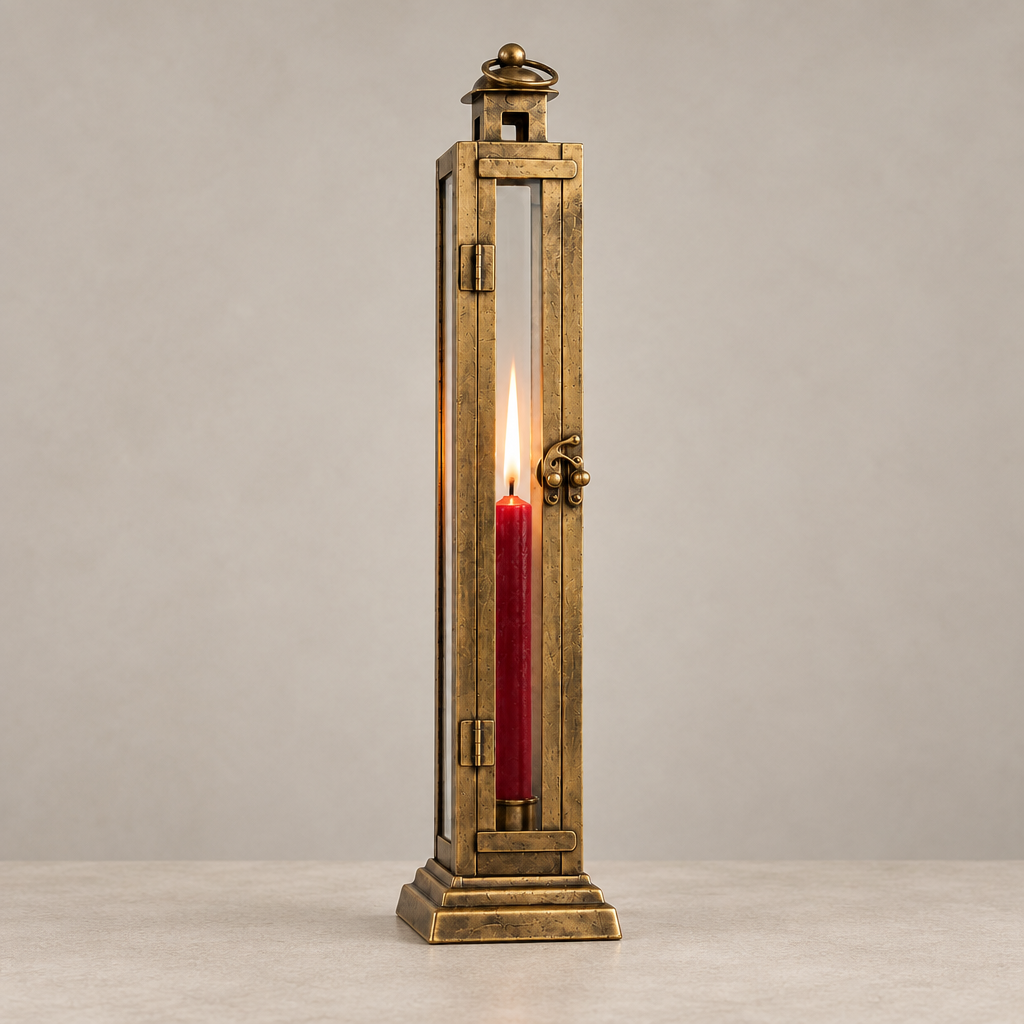 A tall rectangular brass lantern-style candle holder with glass panels, shown lit with a red taper candle inside, set against a neutral gray background.