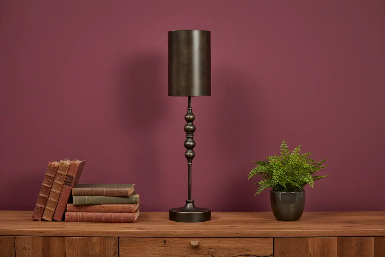 Decorative lamp with books and a plant on a wooden surface against a purple wall