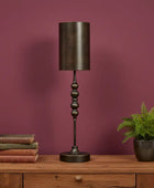 Decorative table lamp with a dark finish on a wooden surface against a purple wall.