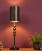Decorative table lamp with a dark shade and base on a wooden surface against a purple wall.