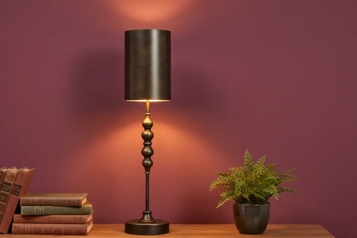 Decorative table lamp with a dark shade and base on a wooden surface against a purple wall.