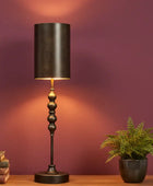 Decorative table lamp with a black shade on a wooden surface against a purple wall.