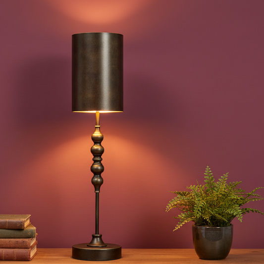 Decorative table lamp with a black shade on a wooden surface against a purple wall.