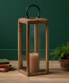 Wooden lantern with a candle and books on a wooden surface against a green wall