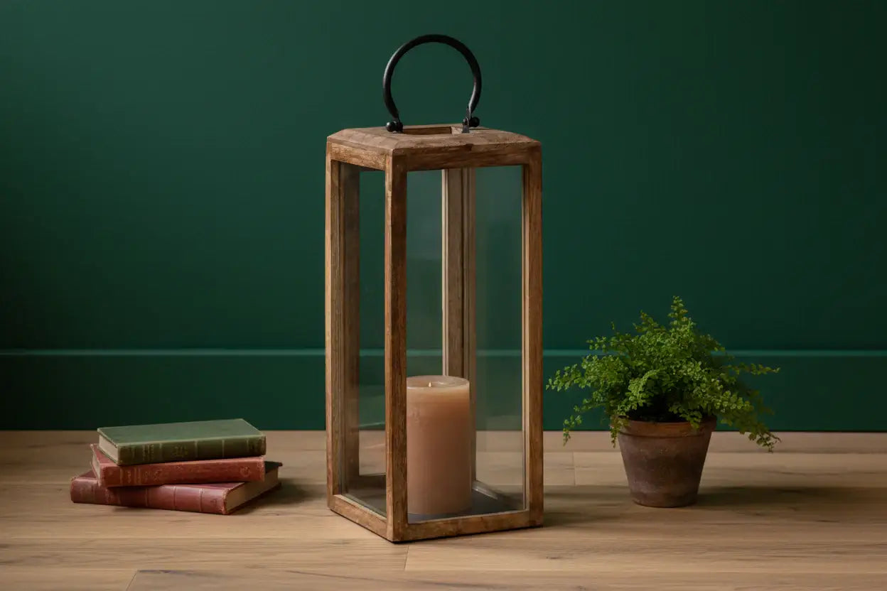 Wooden lantern with a candle and books on a wooden surface against a green wall