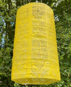 Yellow lace lantern hanging outdoors with green foliage in the background