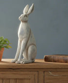 Decorative rabbit statue on a wooden surface with a plant and book in the background.