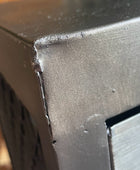 Close-up of a dark gray or black metal corner with visible scratches, dust, and a brushed metallic surface on the adjacent panel.