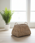 Wicker basket on a wooden floor with a potted plant in the background