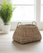 Wicker basket on a wooden floor with a potted plant in the background
