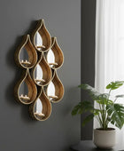 Decorative wall art with teardrop-shaped candle holders on a gray wall with a plant in the foreground.