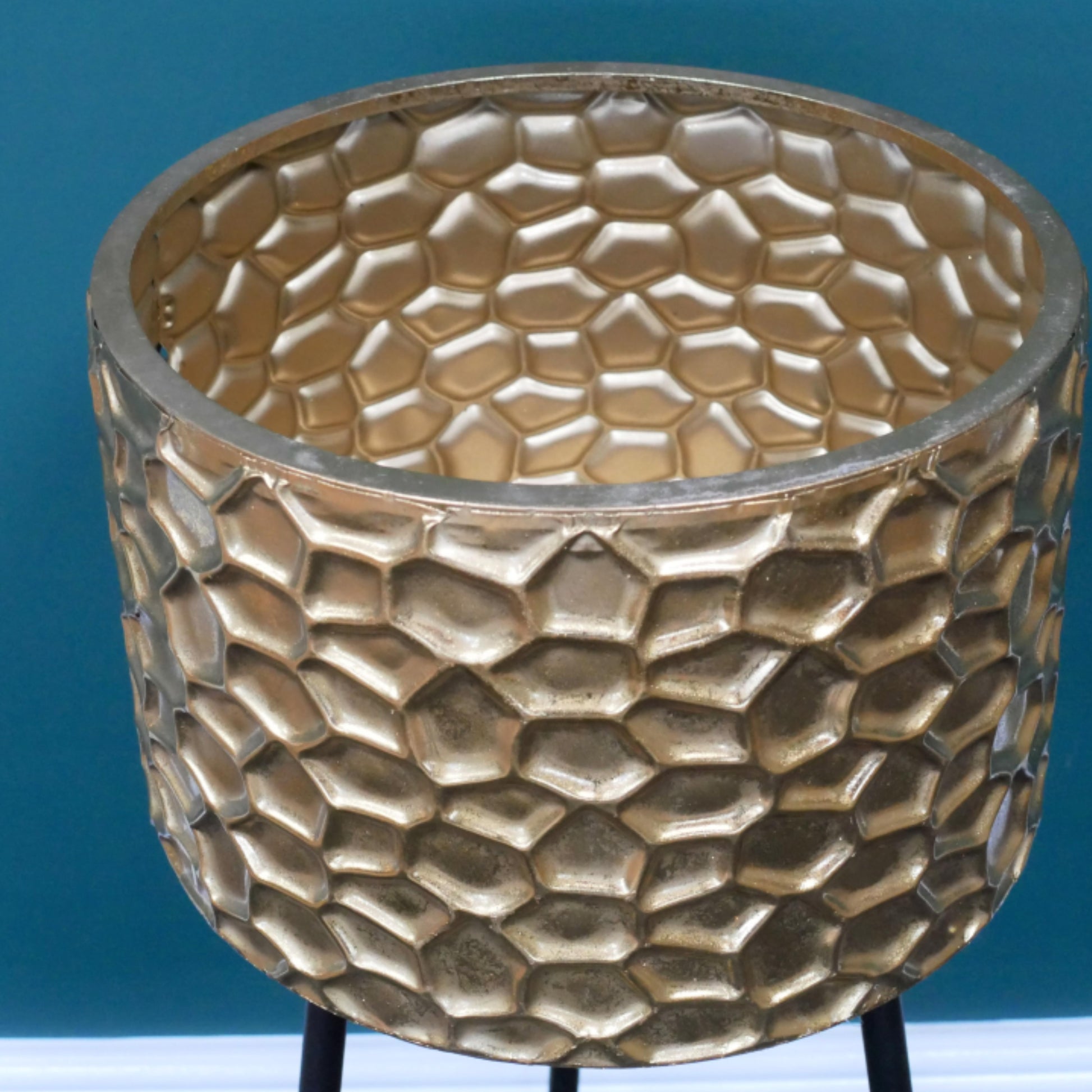 Gold textured planter on a stand against a blue background